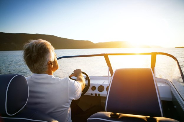 A man drives his boat out on the water towards a sunset, with massive hills appearing on the horizon.